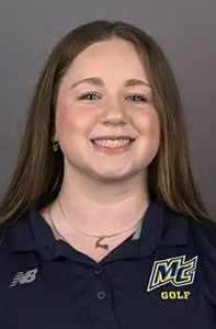 A young woman with straight, light brown hair smiles at the camera. She is wearing a navy blue polo shirt with an MC Golf logo and a New Balance emblem. The background is plain and gray.